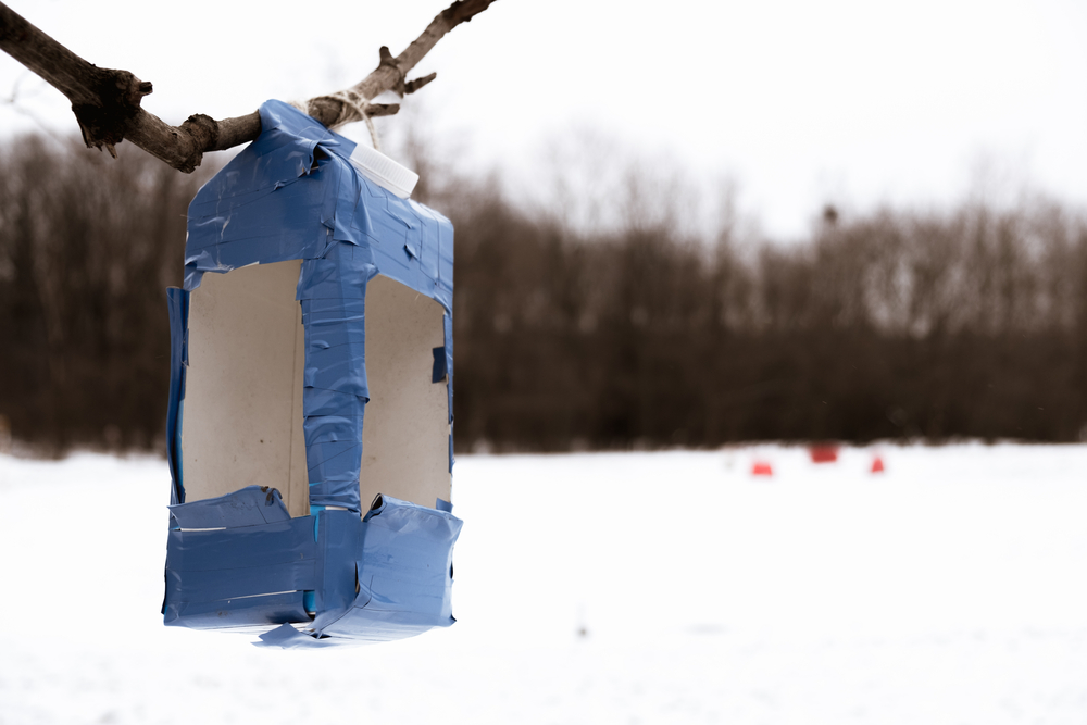 A milk carton bird feeder reinforced with electrical tape