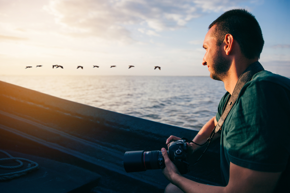 Photographer travelling by boat and watching the birds of the Danube Delta at sunset
